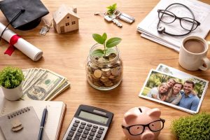 The image presents a clean, realistic scene that symbolizes the progression of finances across different stages of life. Objects such as a diploma, a small house, family photos, savings, and financial tools represent education, career beginnings, family responsibilities, and long-term security. Together, these elements suggest how priorities change over time while maintaining balance and thoughtful planning.