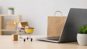 The image visually represents this transformation through a clean and minimalist composition featuring a laptop, shopping bags, and a miniature shopping cart filled with packages. The scene symbolizes the growing influence of the digital economy and the increasing dominance of online purchasing in everyday life. Soft lighting and neutral tones reinforce the modern, efficient, and technology-driven atmosphere associated with contemporary retail.